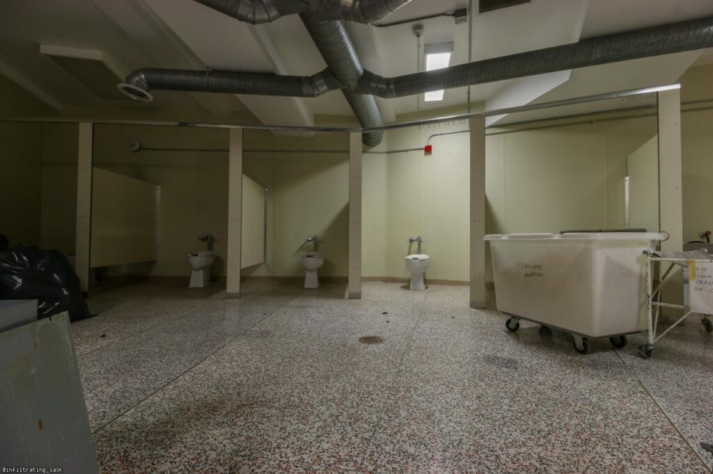 row of toilets in the Valley View Centre. No stall doors separate them. The tile and room is yellowed